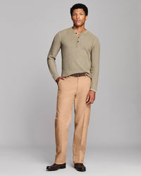 A man modeling a beige ribbed long-sleeve henley shirt and tan trousers against a light gray studio background.