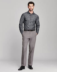 A man modeling a charcoal gray patterned long-sleeve button-down shirt paired with gray trousers, a black belt, and black dress shoes against a light gray studio background.