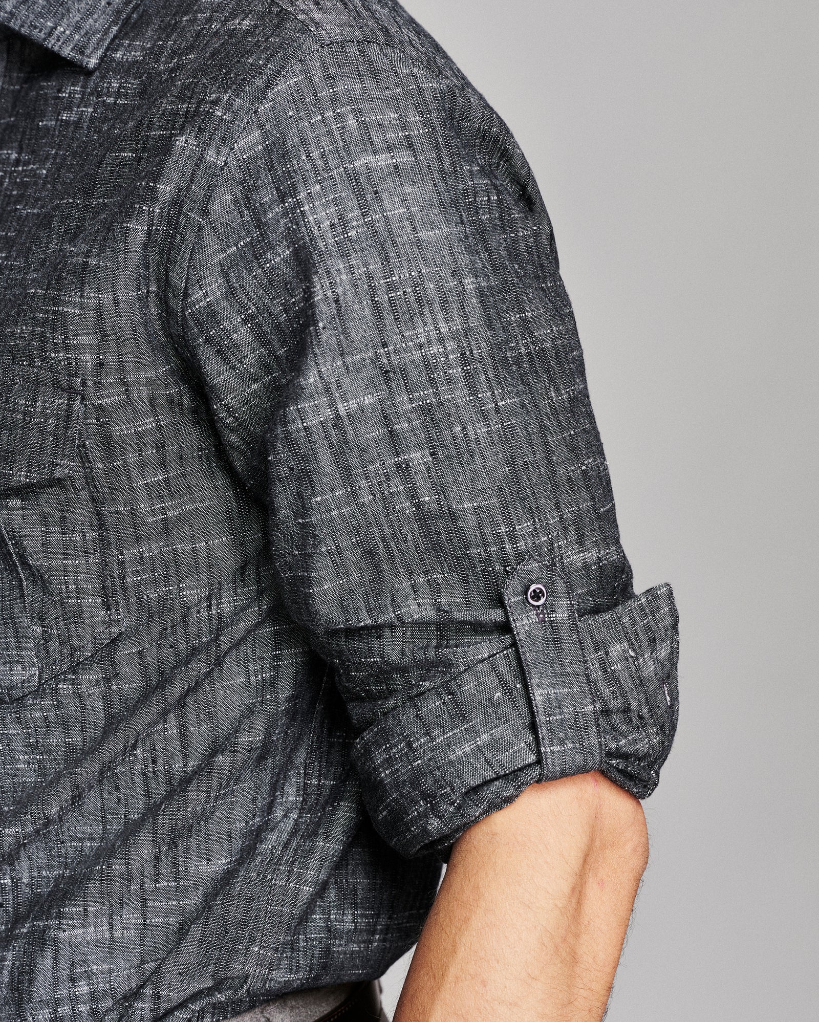 Close-up of a man wearing a dark gray textured short-sleeve shirt with the sleeve rolled up, showing the fabric weave and button cuff detail.