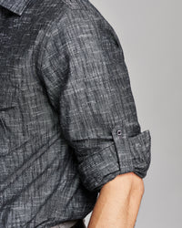 Close-up of a man wearing a dark gray textured short-sleeve shirt with the sleeve rolled up, showing the fabric weave and button cuff detail.