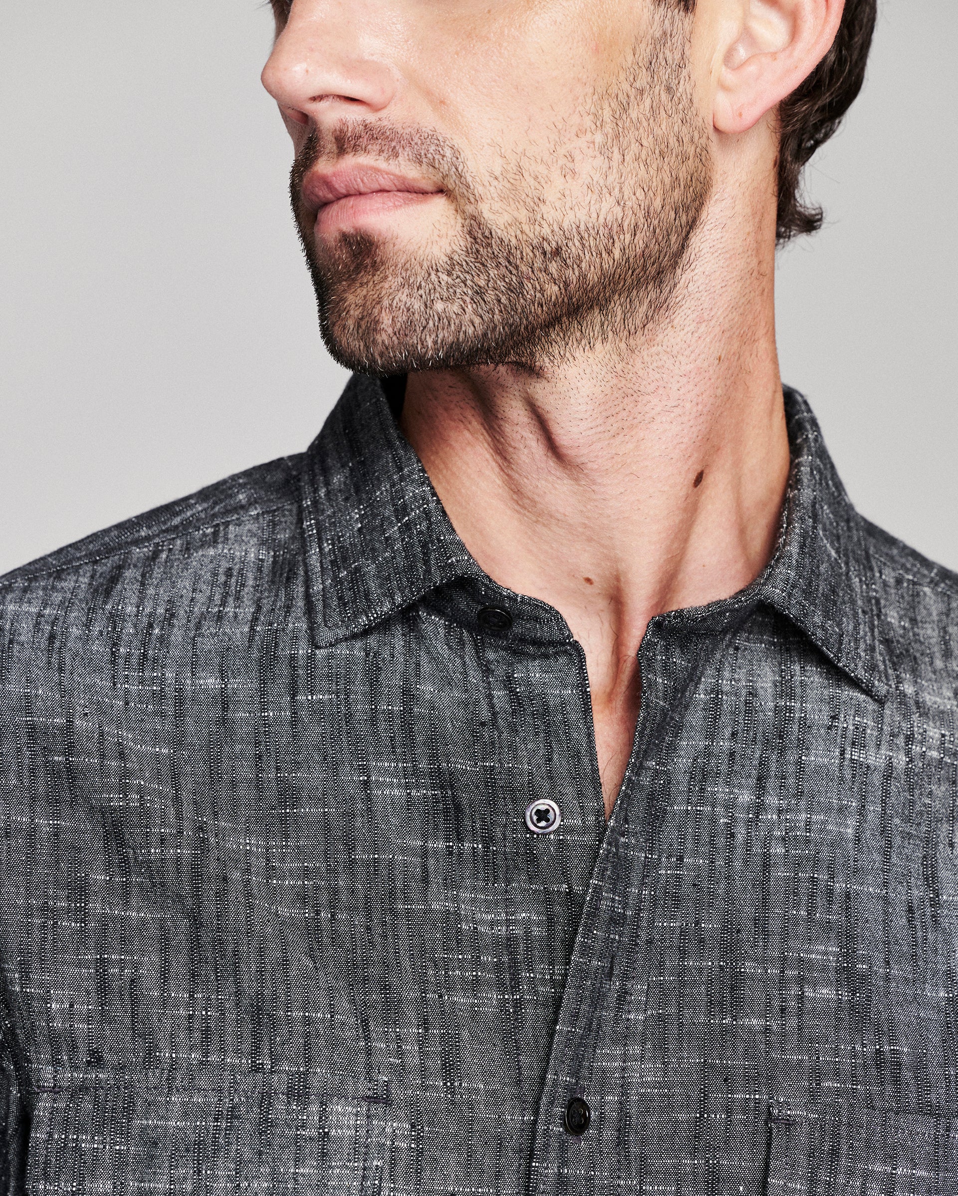 Close-up of a man wearing a dark gray textured button-down shirt, showing the collar, chest area, and part of his face against a light gray background.