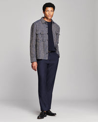 A man modeling a gray textured overshirt jacket over a dark navy crewneck shirt and matching navy trousers, paired with black dress shoes, against a light gray studio background.