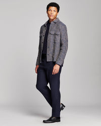 A man modeling a gray and black textured tweed jacket over a dark navy shirt and navy trousers, paired with black dress shoes, against a light gray studio background.