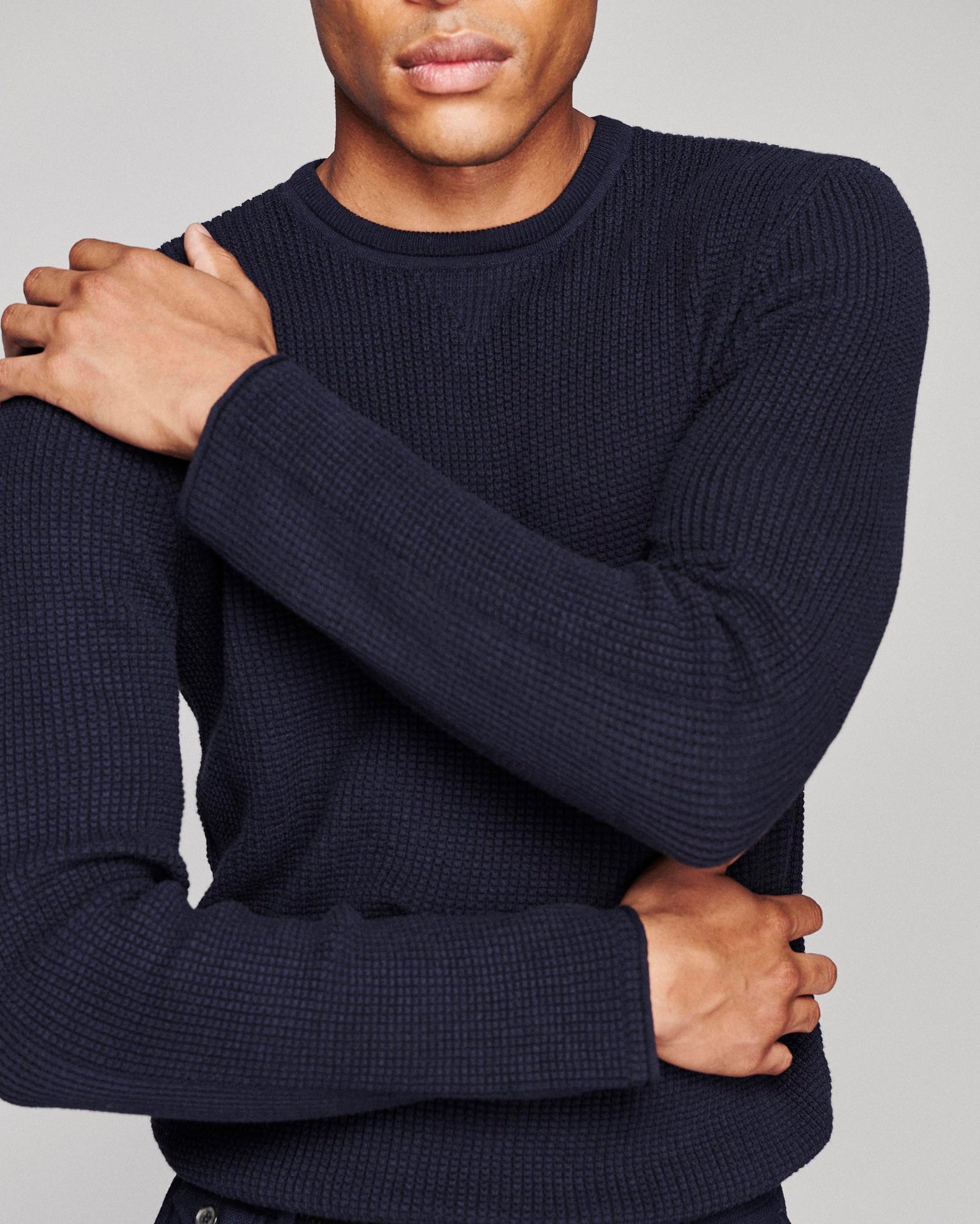 A close-up of a man wearing a dark navy blue waffle-knit crewneck sweater, showing the texture of the knit fabric.