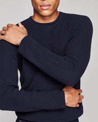 A close-up of a man wearing a dark navy blue waffle-knit crewneck sweater, showing the texture of the knit fabric.