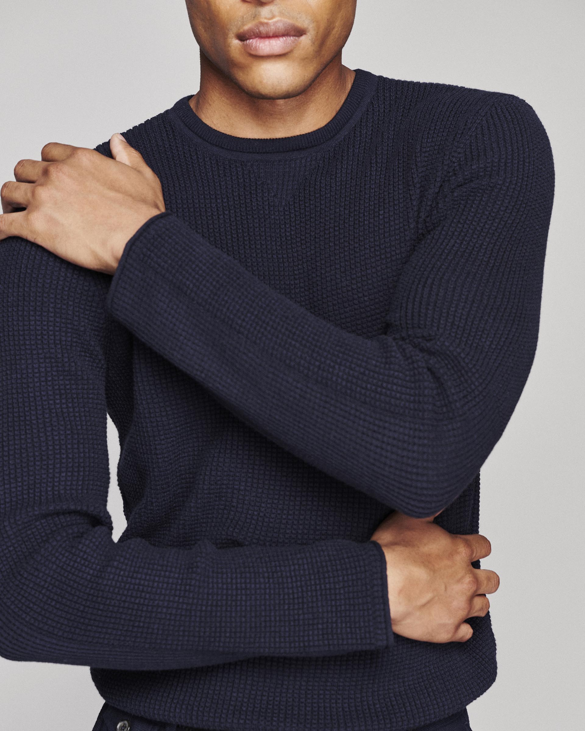 A close-up of a man wearing a dark navy blue waffle-knit crewneck sweater, showing the texture of the knit fabric.