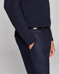 A close-up of a person wearing navy blue textured knit sweater and matching navy trousers with a black belt, shown against a light gray studio background.