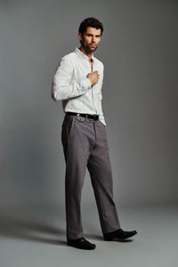 A man modeling a white long-sleeve button-down shirt and gray trousers against a solid gray studio background.