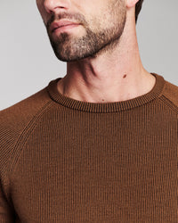 Close-up of a man wearing a brown ribbed crewneck sweater, showing the texture of the knit fabric and the collar.