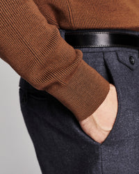Close-up of a person wearing a brown ribbed knit sweater, a black leather belt, and dark charcoal gray textured trousers with a hand in the pocket.