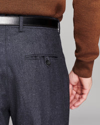 Close-up of a person wearing dark charcoal gray textured trousers with a black belt and a brown knit sweater, showing the back pocket detail.