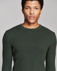 A man wearing a dark forest green textured knit crewneck sweater, shown from the chest up against a solid light gray background.