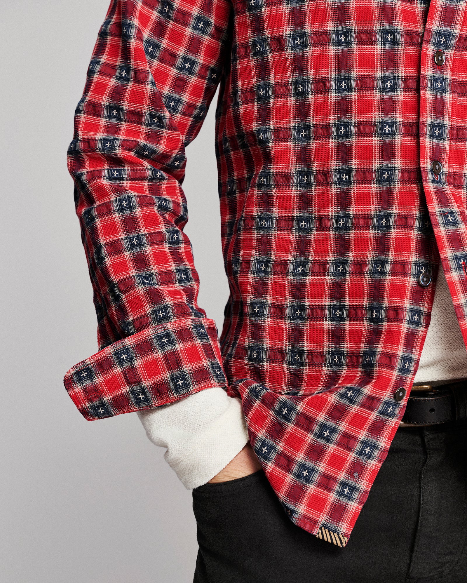 A close-up of a red, navy, and white plaid flannel shirt worn by a model, with the cuffs rolled up and a white undershirt visible.