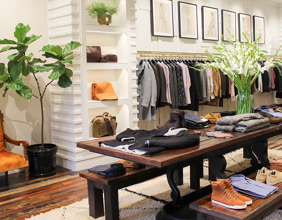 Interior of a clothing store with racks of clothes, a wooden bench, and decorative elements.