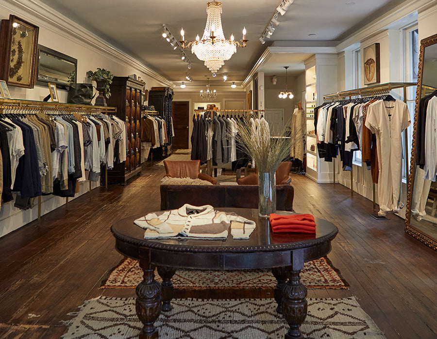 Luxury clothing store interior with wooden tables, chairs, and racks of clothes.