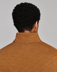 Back view of a person with curly black hair wearing a mustard brown ribbed knit mock neck sweater against a light gray background.