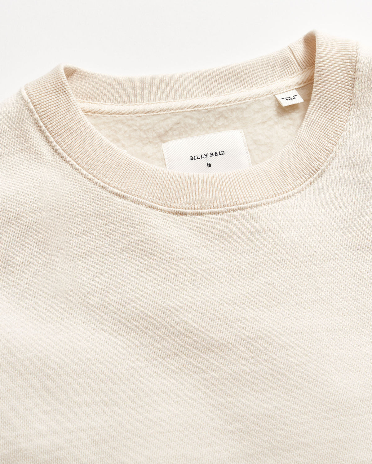 Close-up of a beige sweater with a brand label on a white background