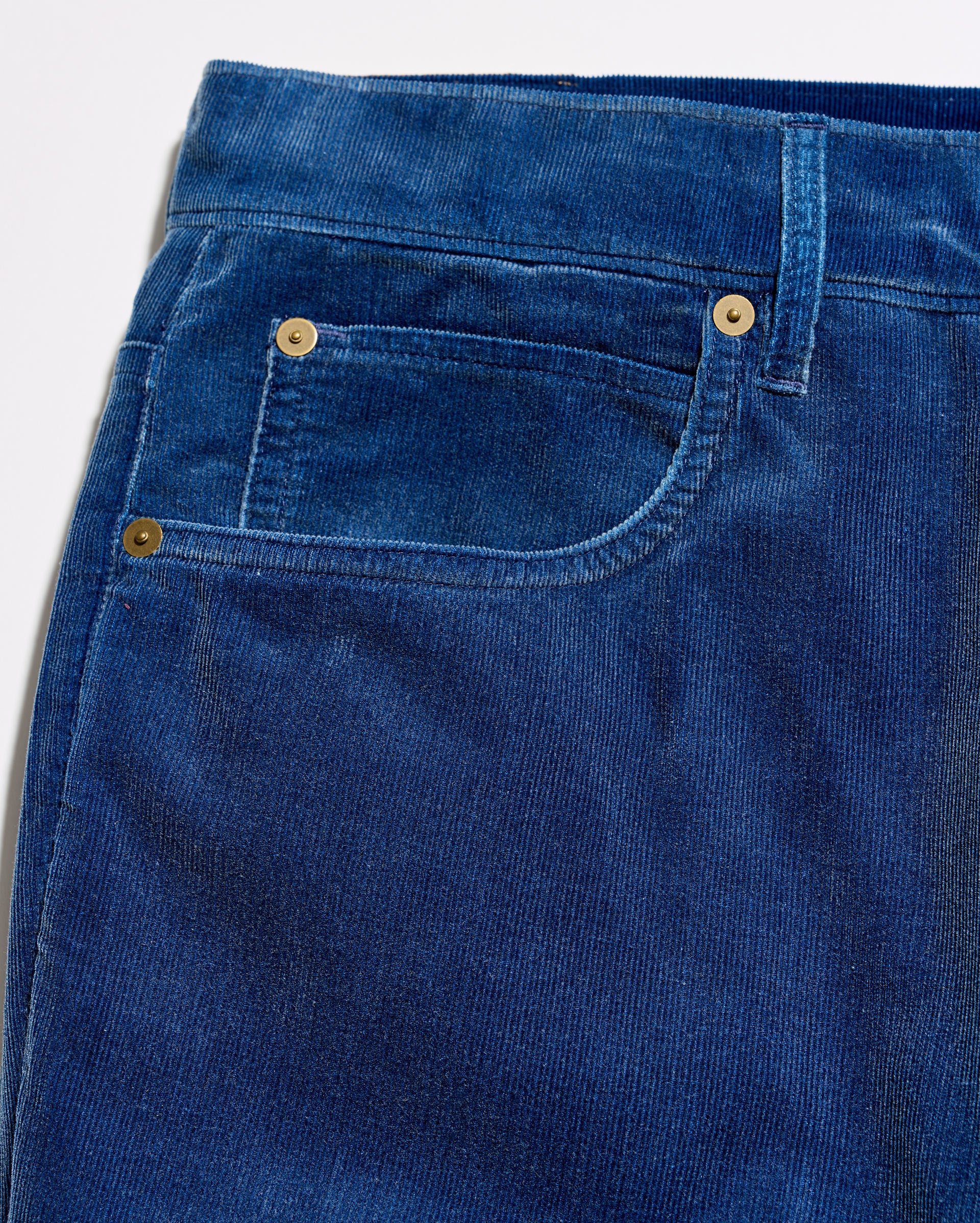 Close-up of a pair of blue corduroy jeans showing the front pocket, button, and rivet details.