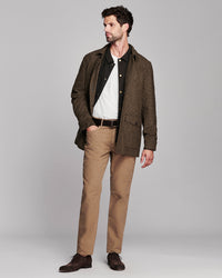 A man modeling a brown textured overshirt over a black polo shirt and white tee, paired with tan trousers and dark brown leather shoes, against a solid gray studio background.