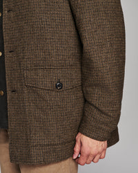 Close-up of a brown and beige houndstooth patterned jacket with a buttoned flap pocket, worn by a model.