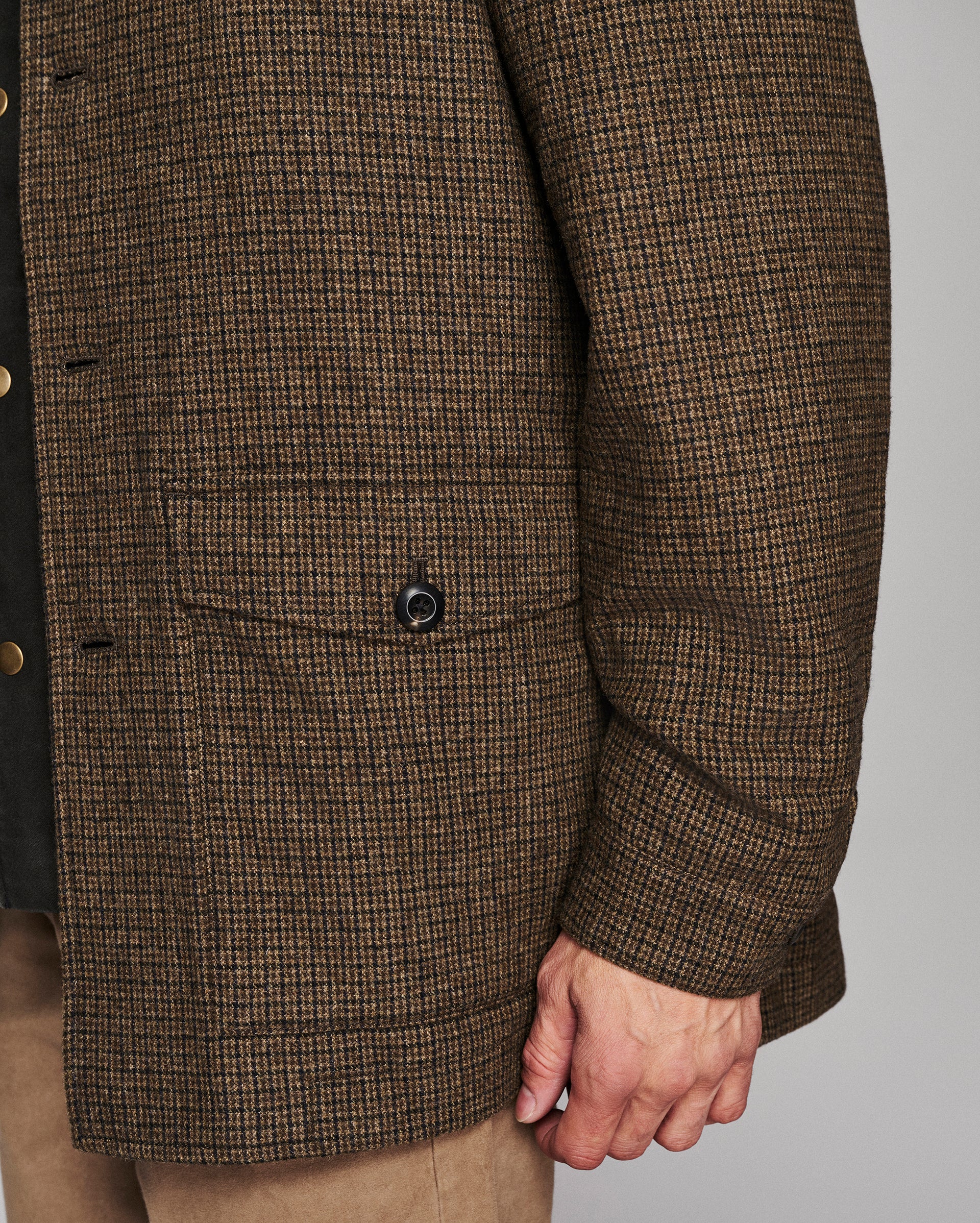 Close-up of a brown and beige houndstooth patterned jacket with a buttoned flap pocket, worn by a model.
