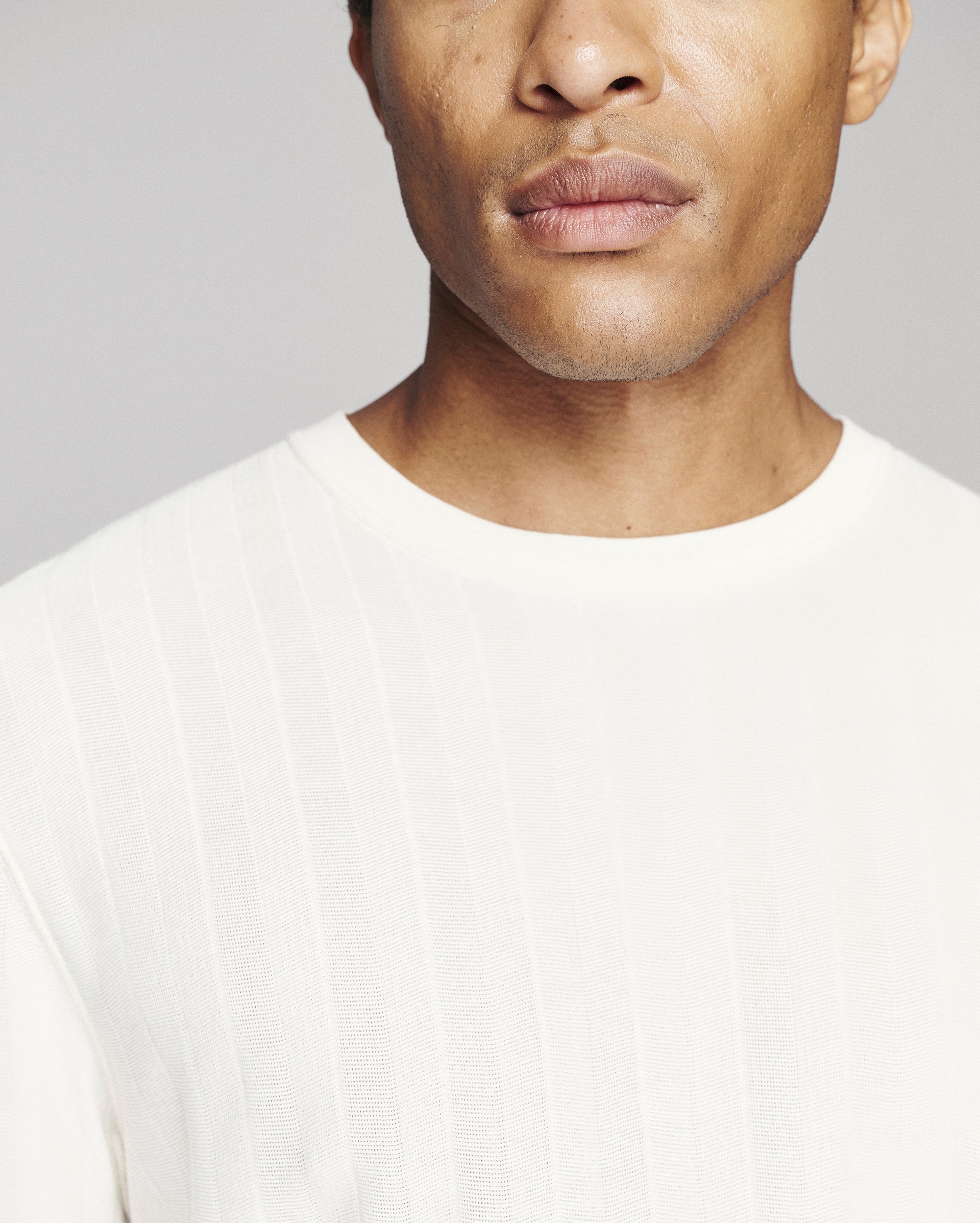 Close-up of a man wearing a white ribbed knit crewneck sweater against a light gray background.
