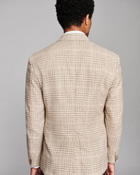 A man viewed from behind wearing a beige and brown plaid blazer over a white collared shirt, set against a solid gray studio background.