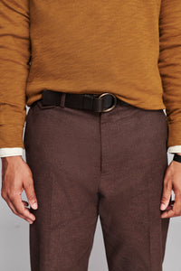 A close-up of a person wearing textured brown trousers, a black leather belt with a silver-tone oval buckle, and a mustard yellow knit sweater.