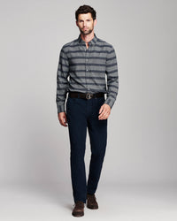 A man modeling a gray and black striped long-sleeve button-down shirt, paired with dark navy trousers, a black belt, and brown dress shoes, against a light gray studio background.