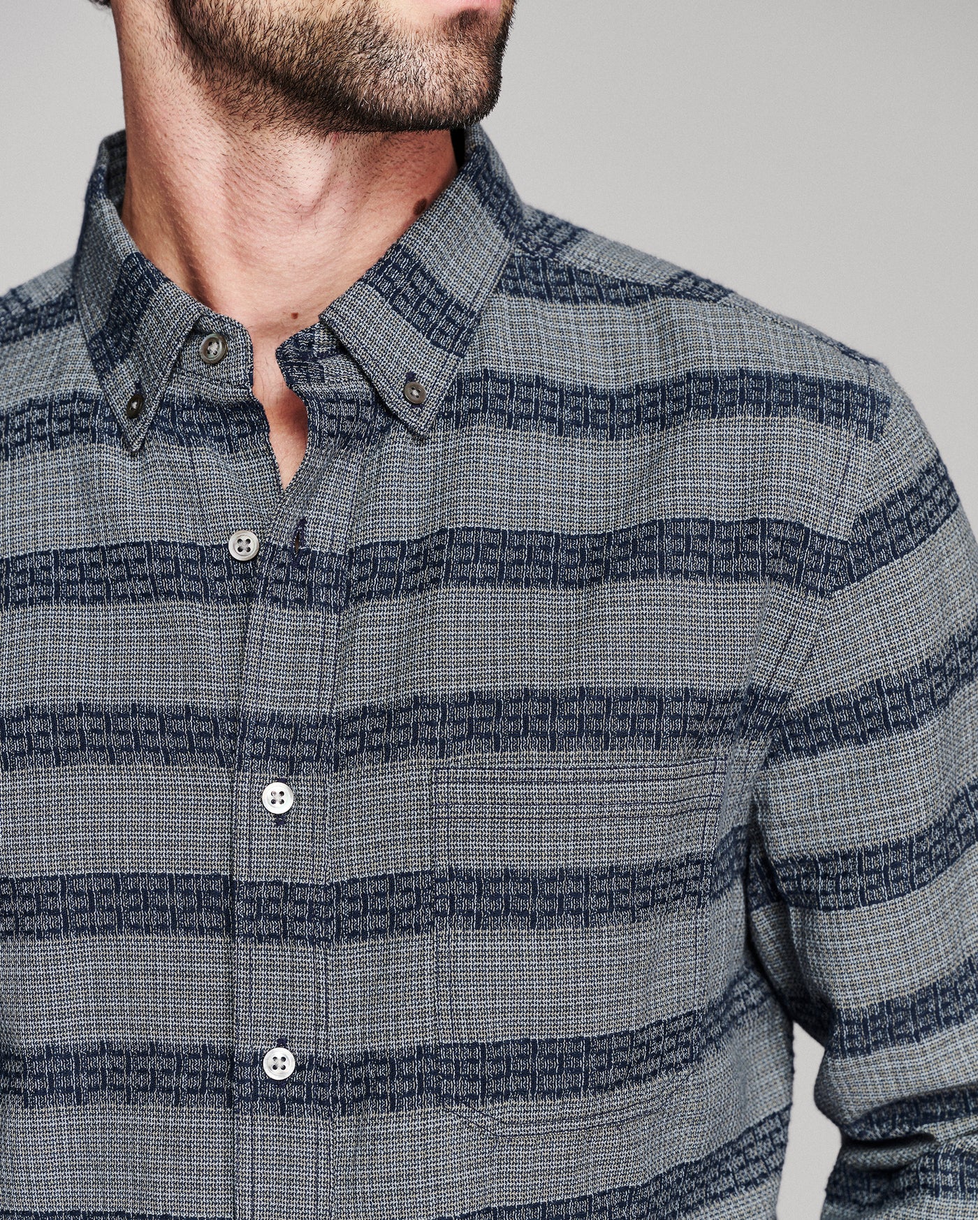 A close-up of a man wearing a gray and navy striped button-down shirt with a textured woven pattern.