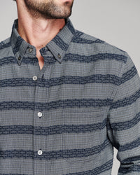 A close-up of a man wearing a gray and navy striped button-down shirt with a textured woven pattern.