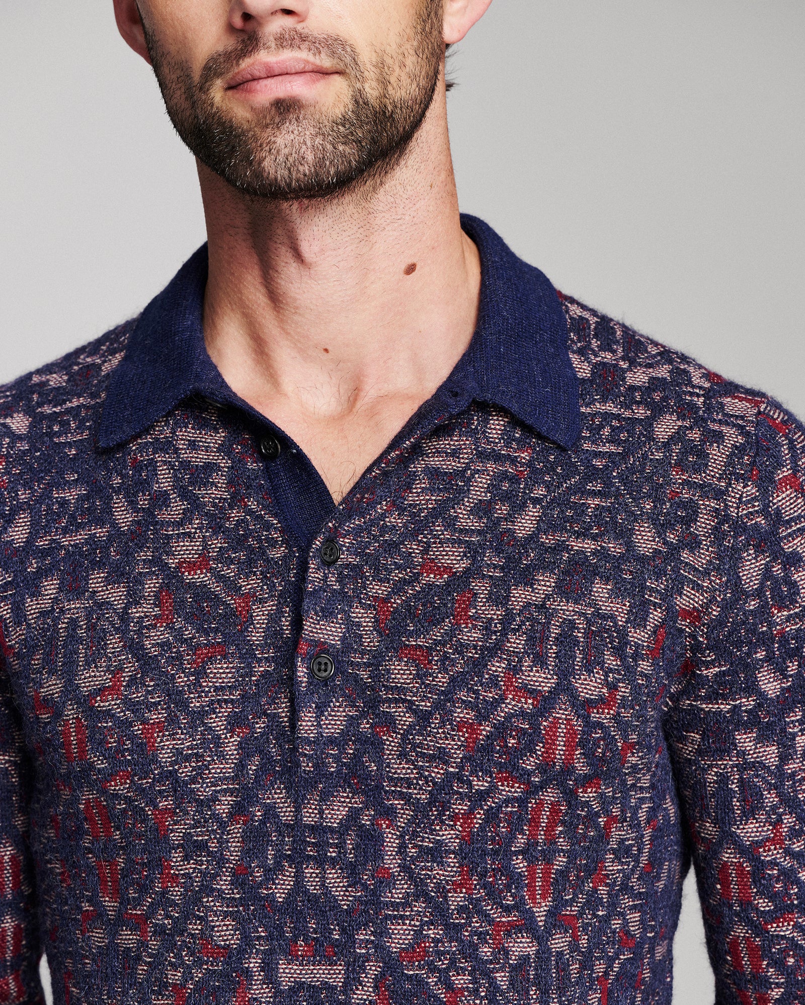 A close-up of a man wearing a navy blue knit polo shirt with a red and beige geometric pattern.