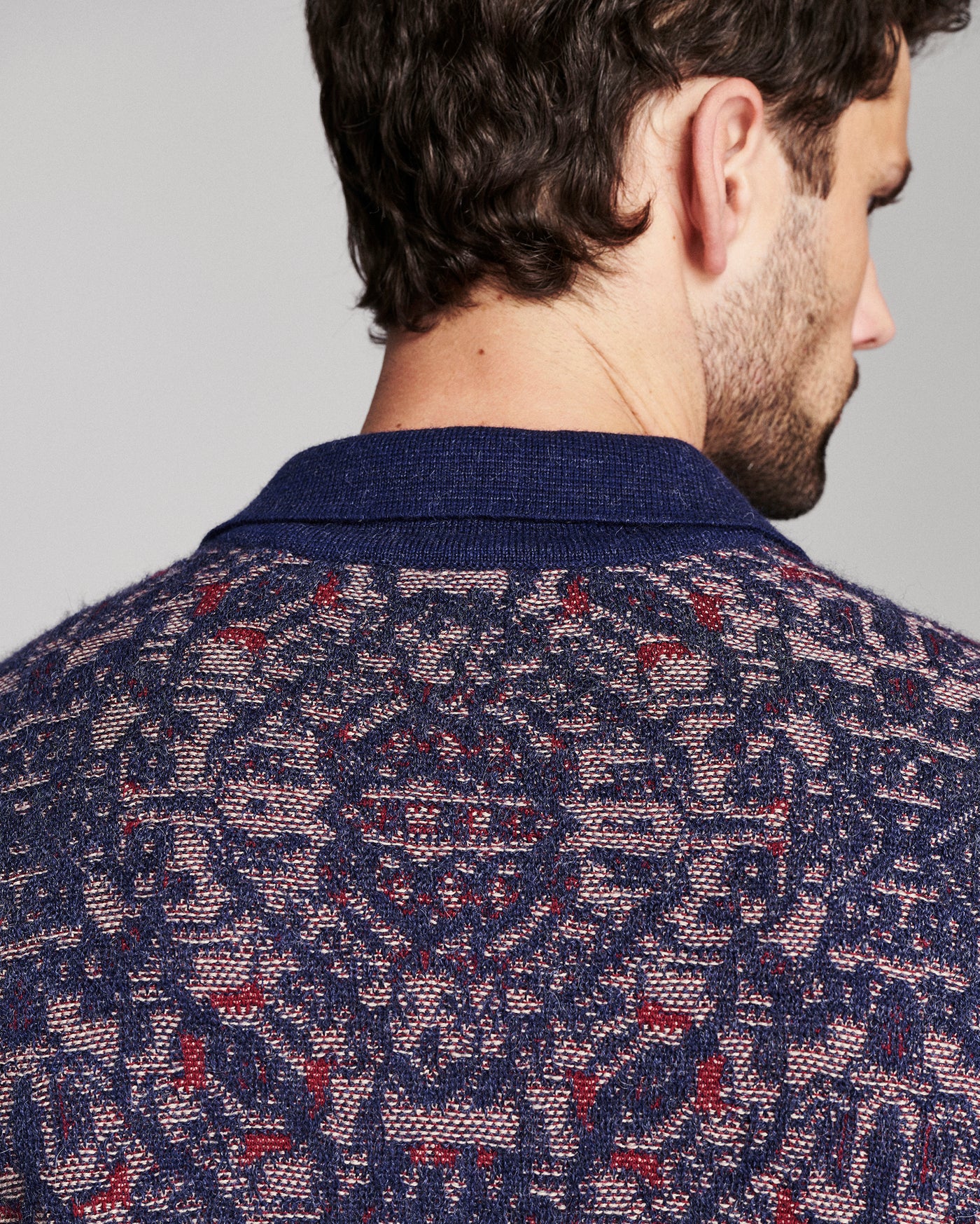 Close-up back view of a man wearing a navy blue knit sweater with a red and beige geometric pattern.