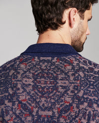 Close-up back view of a man wearing a navy blue knit sweater with a red and beige geometric pattern.