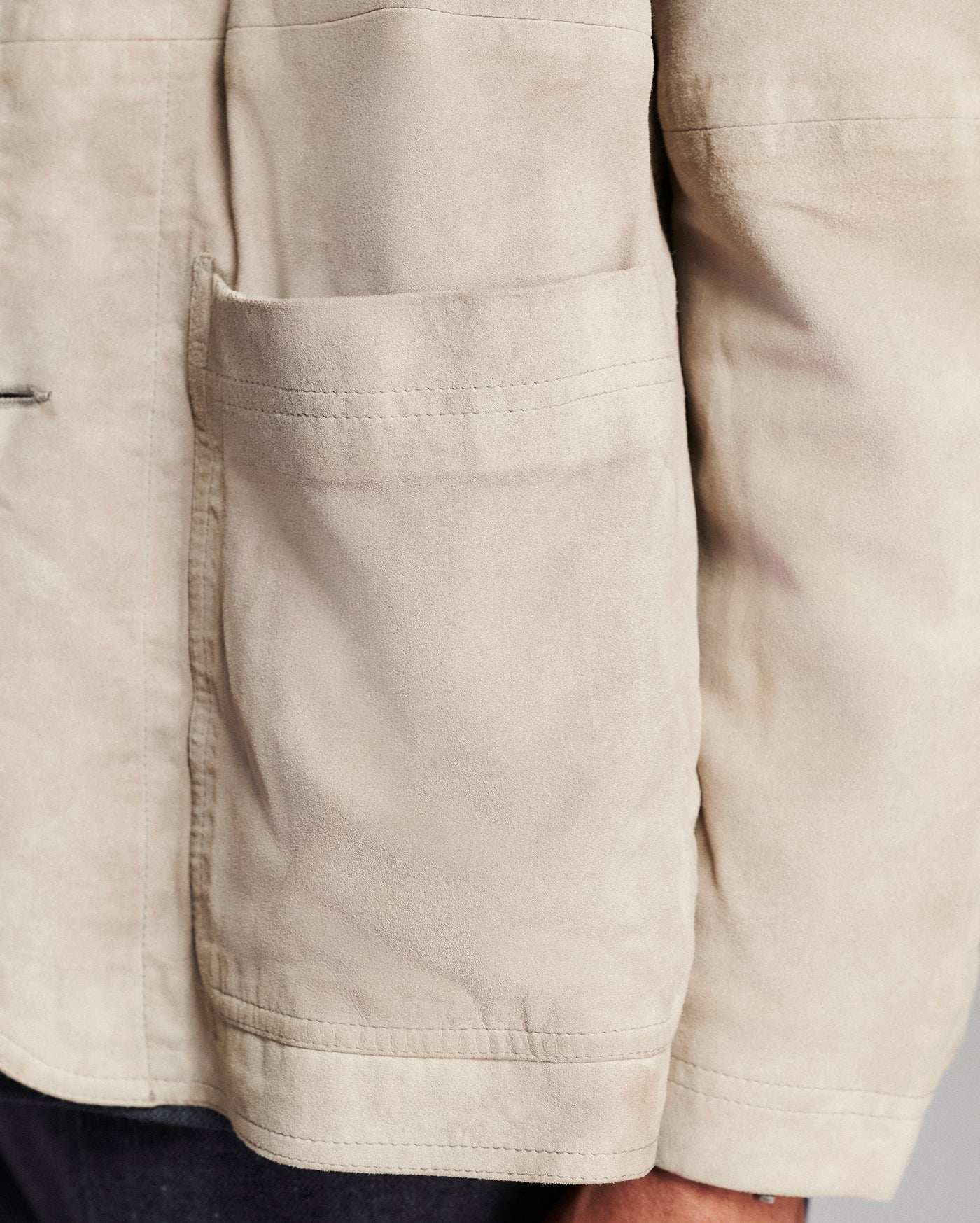 Close-up of a beige canvas utility jacket with a front patch pocket, worn by a model.