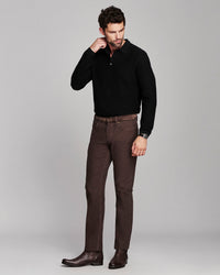 A man modeling a black ribbed knit polo shirt and dark brown trousers with brown leather boots, standing against a solid light gray studio background.