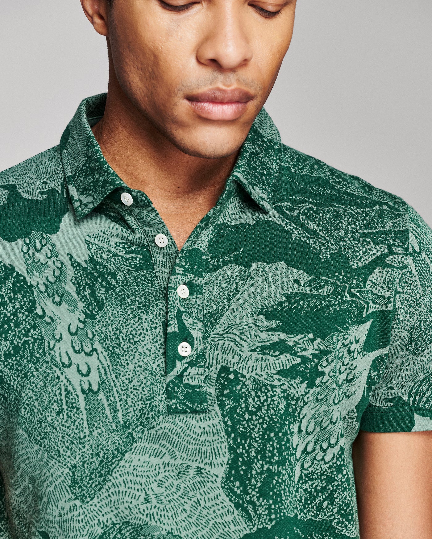 A close-up of a man wearing a short-sleeve polo shirt with a detailed green and teal dragon pattern, featuring a buttoned collar and chest pocket.