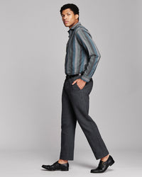 A man modeling a charcoal gray striped button-down shirt and dark gray trousers with black dress shoes, photographed against a solid light gray studio background.