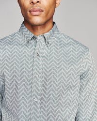 A close-up of a man wearing a light gray and white patterned button-down shirt, showing the collar, front buttons, and part of the chest against a plain gray background.