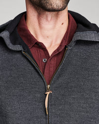 Close-up of a man wearing a dark gray ribbed zip-up hoodie with a black hood lining, layered over a burgundy ribbed button-up shirt.