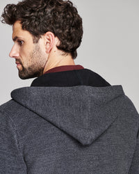 A man shown from the back wearing a dark gray textured hooded sweater over a black shirt with a burgundy collar, against a solid light gray background.