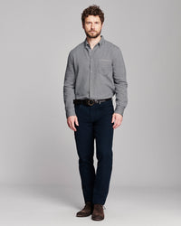 A man modeling a gray long-sleeve button-down shirt with a chest pocket, paired with dark navy jeans and brown leather shoes, against a solid gray studio background.