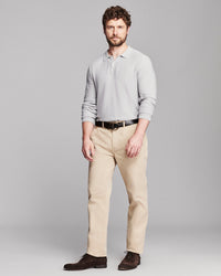 A man modeling a light gray long-sleeve polo shirt, beige trousers, a black belt, and dark brown dress shoes against a solid gray studio background.