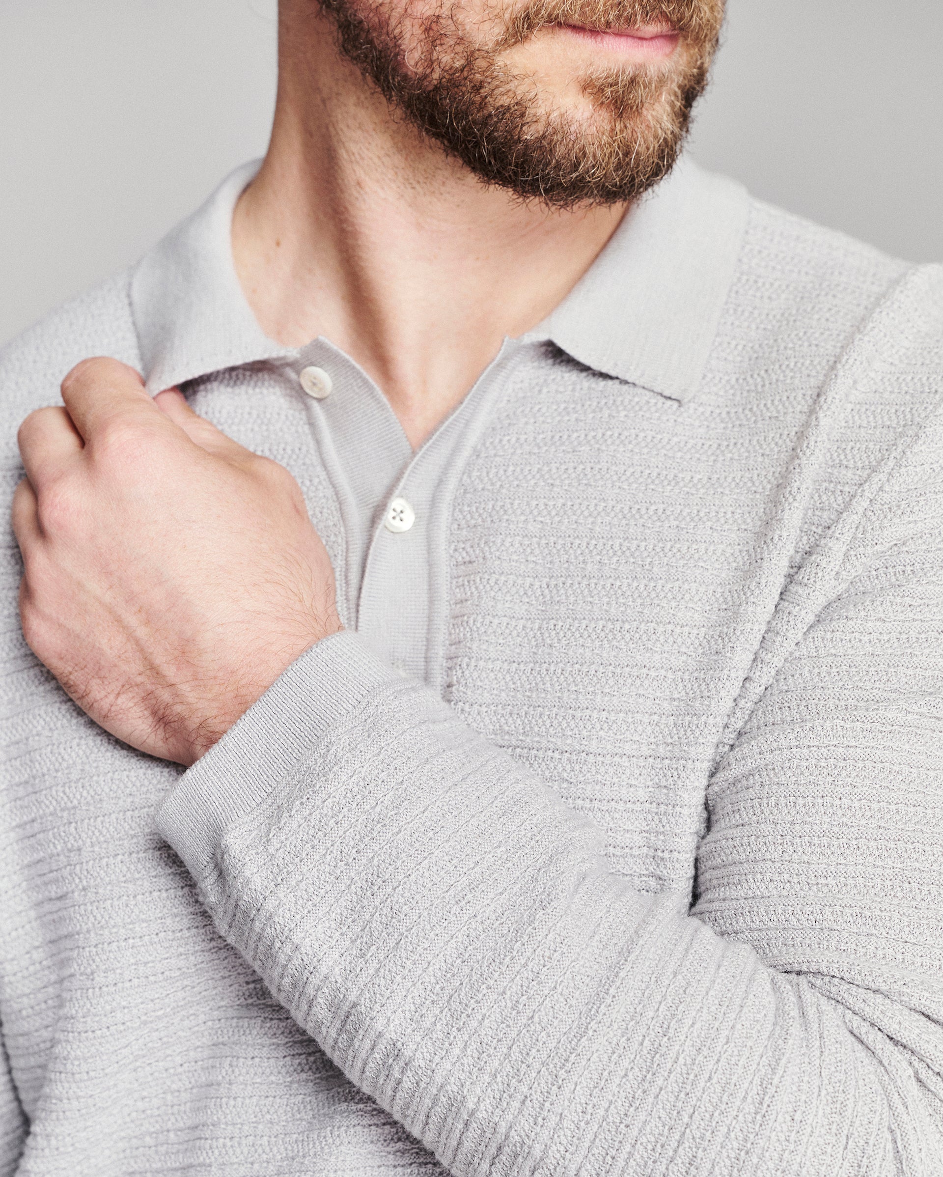Close-up of a man wearing a light gray ribbed knit polo shirt, showing the collar, buttons, and textured fabric on his chest and arm.