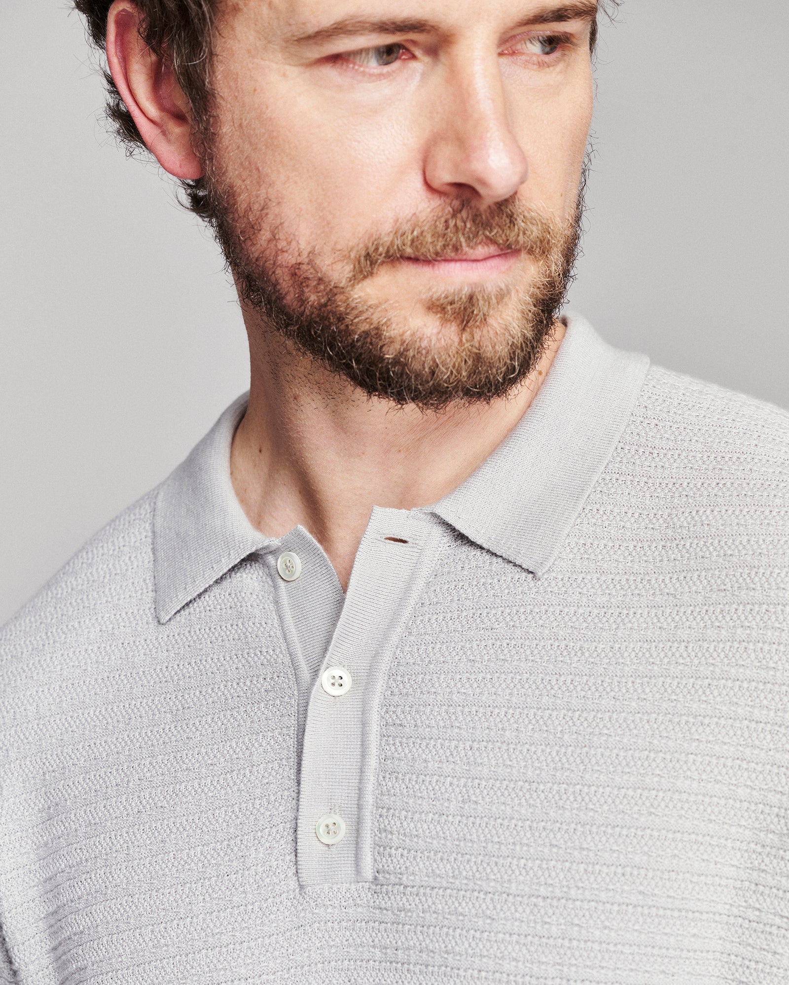 Close-up of a man wearing a light gray textured knit polo shirt against a neutral gray background.