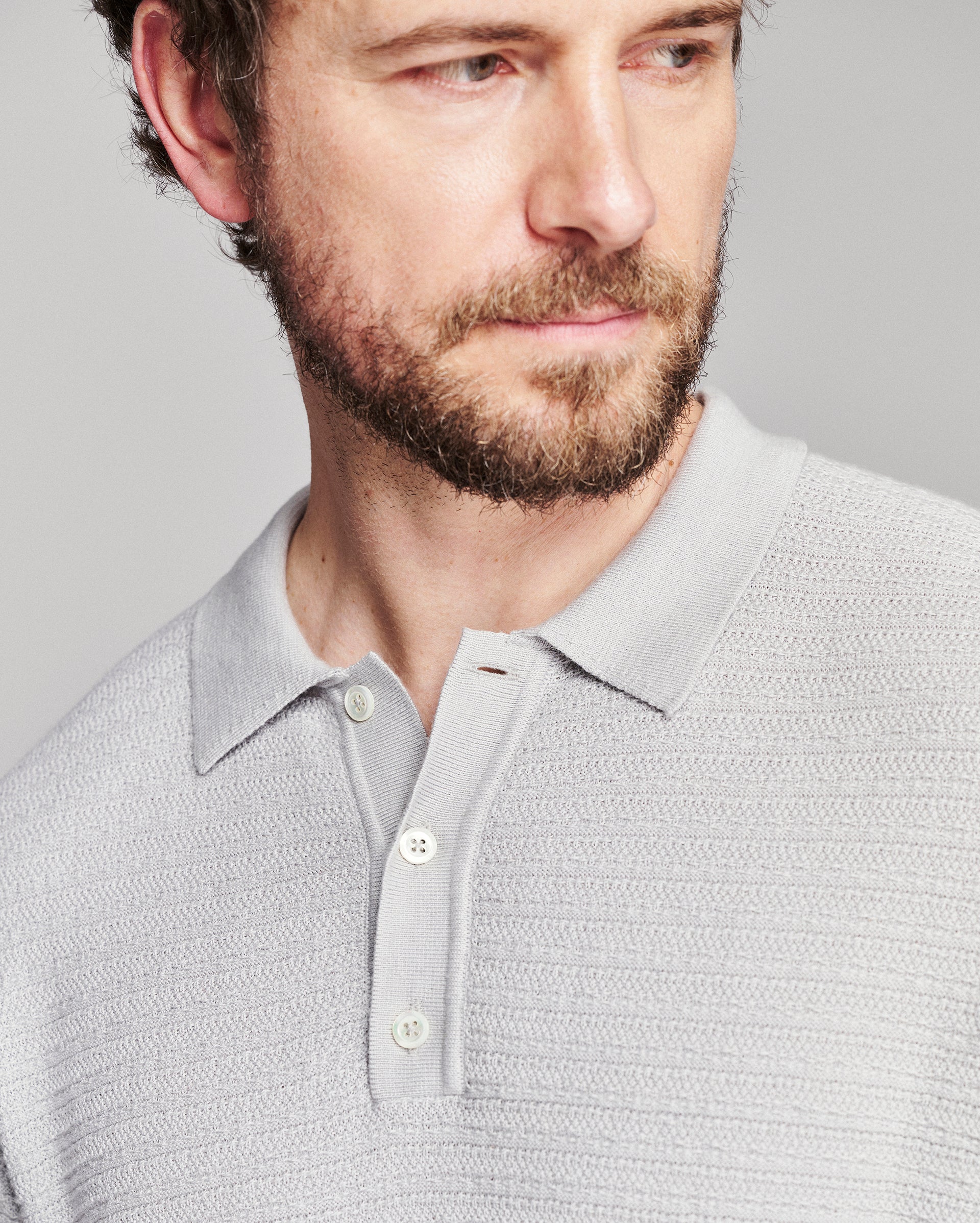 Close-up of a man wearing a light gray textured knit polo shirt against a neutral gray background.