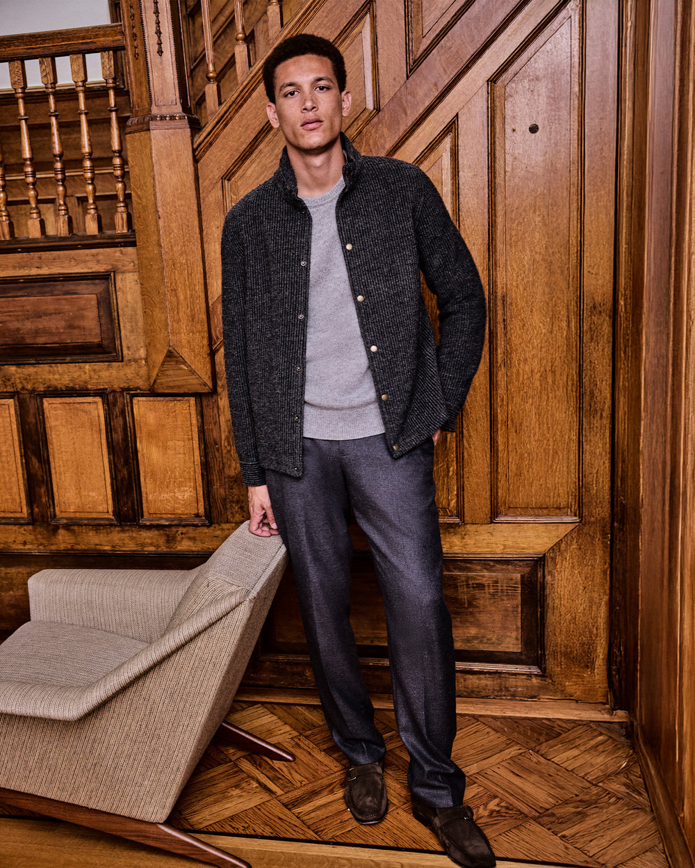 Man standing in a room with wooden paneling and a chair.