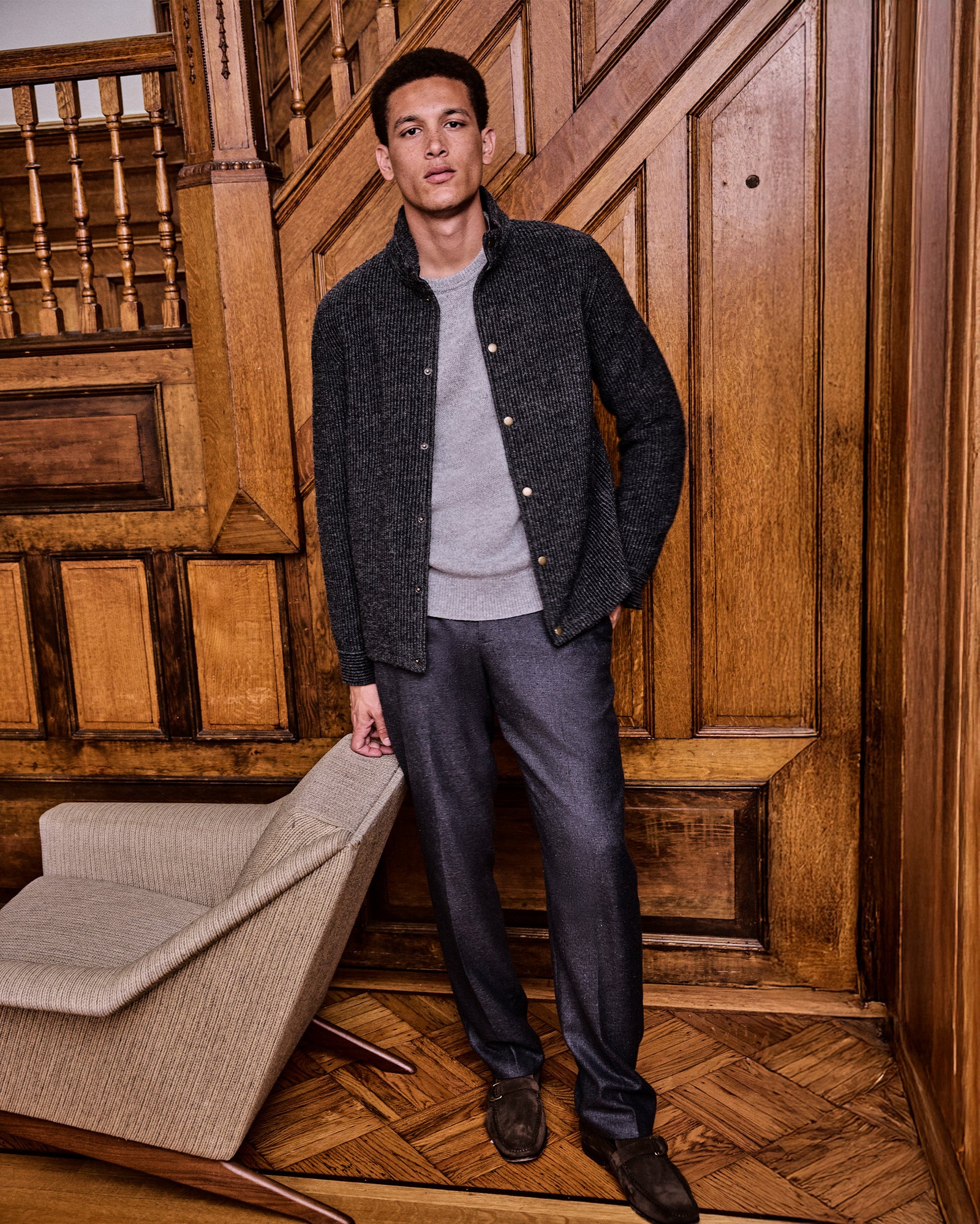 Man standing in a room with wooden paneling and a chair.