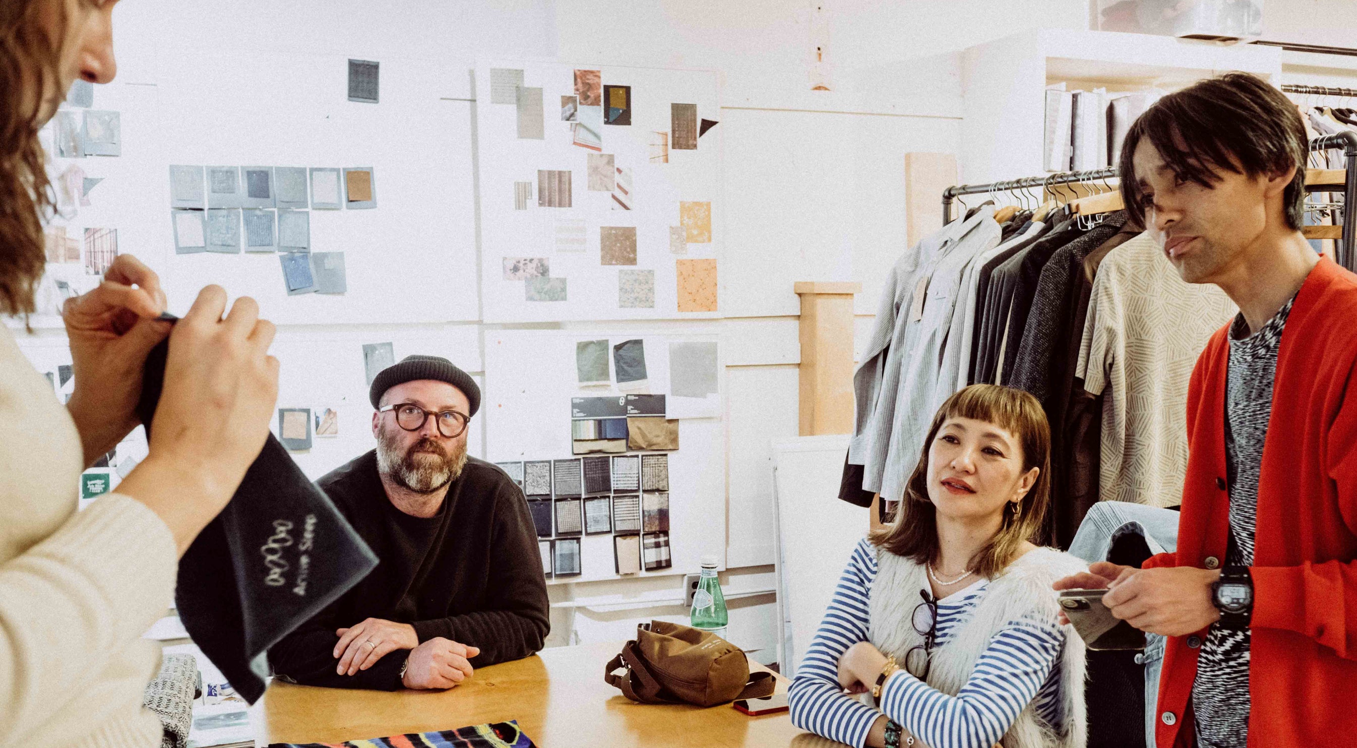 Group of people in a casual setting with clothing racks and a moodboard in the background.