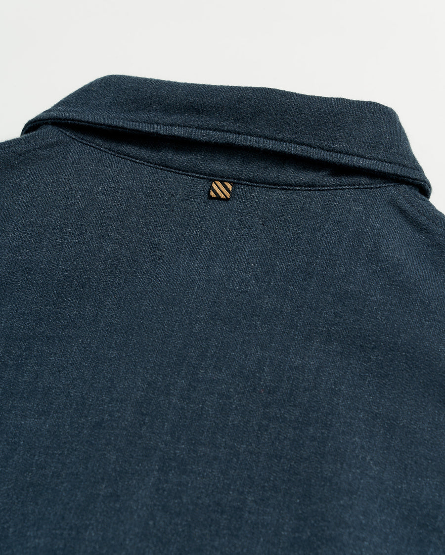 Close-up of the back of a dark blue collared shirt, showing a small, striped loop detail just below the collar on a plain white background.